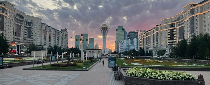 Astana city view featuring Bayterek Tower, modern buildings, and flower gardens at sunset, Kazakhstan landmark.