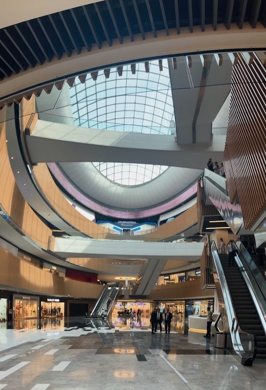Inside Tashkent City Mall: Modern architecture, escalators, shops, and a large skylight. Shopping in Uzbekistan.