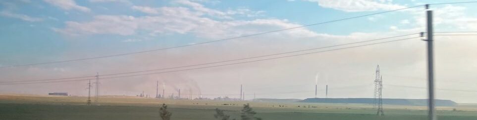 , Kazakhstan landscape with distant industrial chimneys and power lines under a blue sky with clouds.