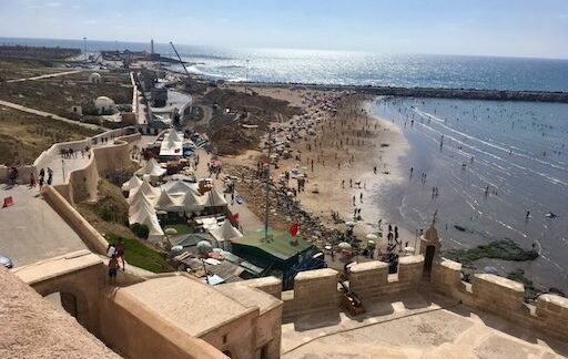 Rabat-Salé beach view: Sandy beach, blue ocean, people enjoying the sun near the old city walls in Morocco.